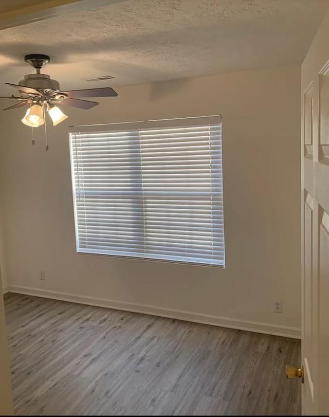 unfurnished room featuring ceiling fan, plenty of natural light, a textured ceiling, and wood finished floors