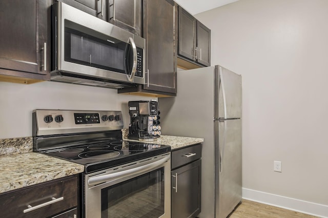 kitchen with light stone countertops, baseboards, stainless steel appliances, dark brown cabinetry, and light wood-style floors