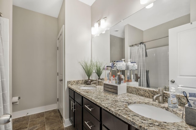 bathroom featuring a tile shower, double vanity, baseboards, and a sink