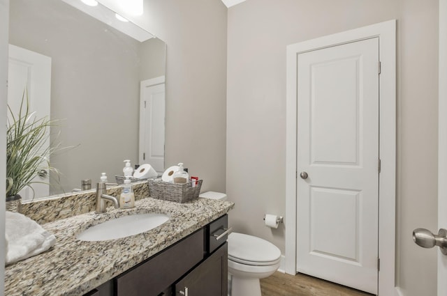 half bathroom with toilet, vanity, and wood finished floors