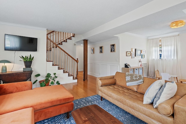 living room featuring ornamental molding, wood finished floors, stairway, wainscoting, and a decorative wall