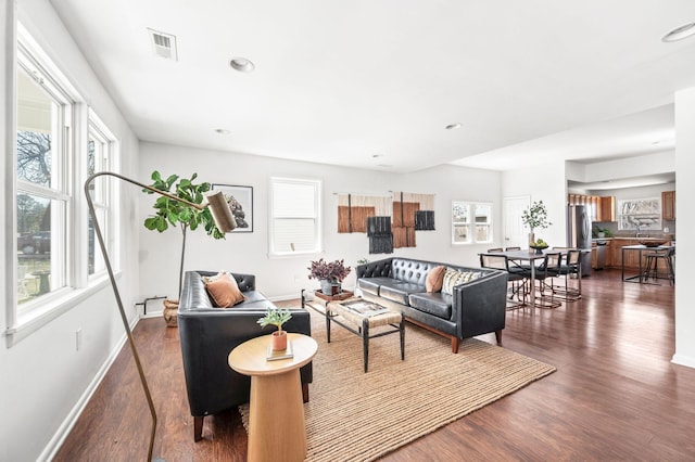 living room with a wealth of natural light, visible vents, and dark wood-type flooring