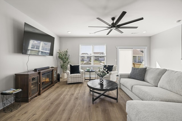 living room featuring visible vents, a ceiling fan, a glass covered fireplace, wood finished floors, and baseboards