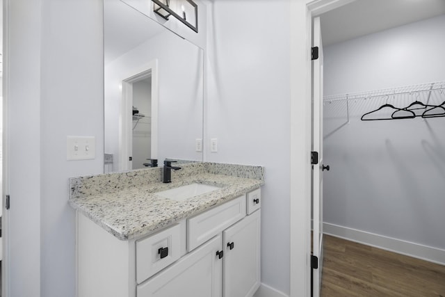 bathroom featuring a walk in closet, baseboards, wood finished floors, and vanity
