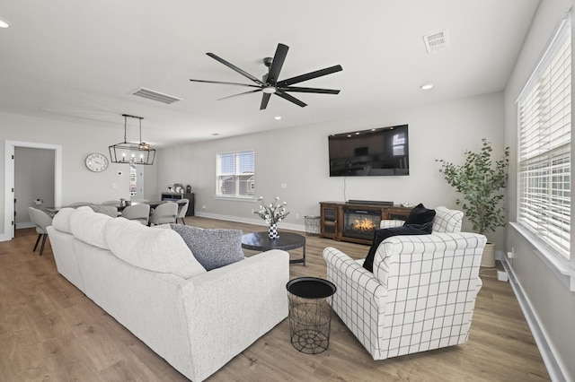 living area with a glass covered fireplace, wood finished floors, a ceiling fan, and visible vents