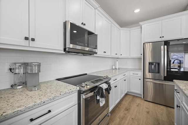 kitchen featuring light wood finished floors, decorative backsplash, white cabinets, and appliances with stainless steel finishes