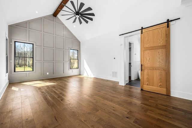 unfurnished living room with high vaulted ceiling, a barn door, a decorative wall, ceiling fan, and dark wood-style flooring