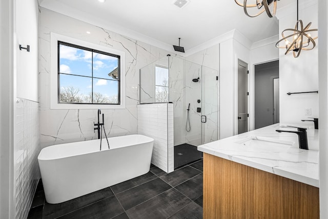 bathroom with a marble finish shower, a freestanding bath, a notable chandelier, tile walls, and a sink