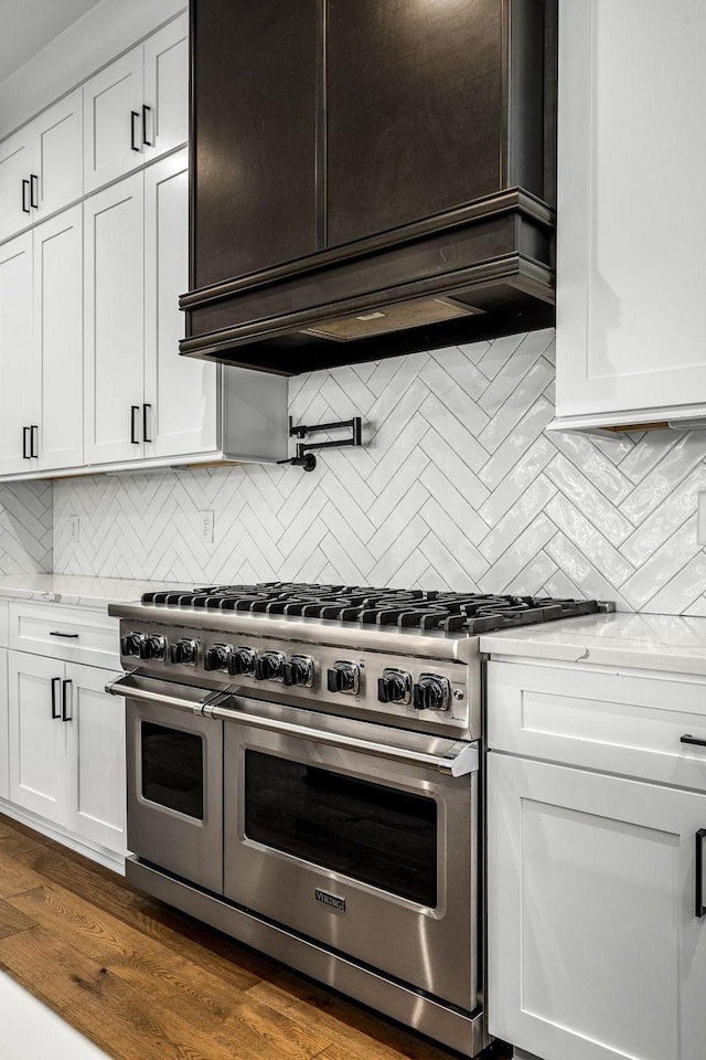 kitchen featuring range with two ovens, decorative backsplash, light stone counters, and white cabinetry