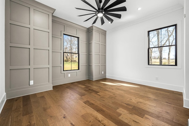 unfurnished room featuring a ceiling fan, wood finished floors, crown molding, a decorative wall, and baseboards