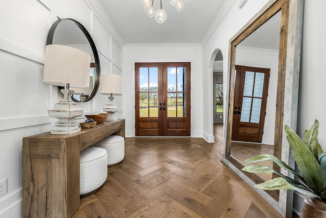 foyer with ornamental molding, french doors, arched walkways, baseboards, and a chandelier