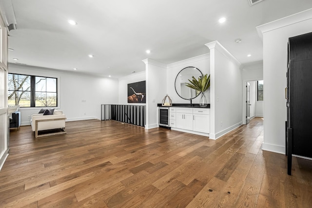 unfurnished living room featuring baseboards, wine cooler, ornamental molding, recessed lighting, and wood-type flooring