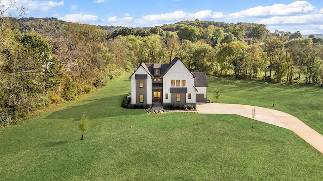 modern farmhouse style home with driveway, a forest view, a front yard, and board and batten siding