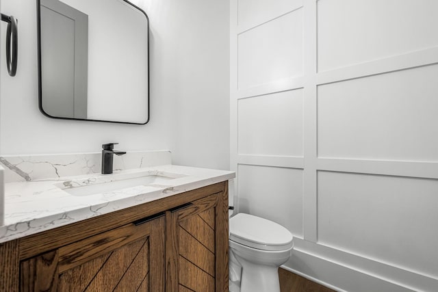 half bath featuring vanity, toilet, and wood finished floors