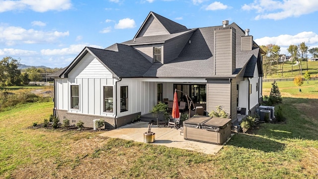 back of property with board and batten siding, a hot tub, a chimney, a yard, and a patio area