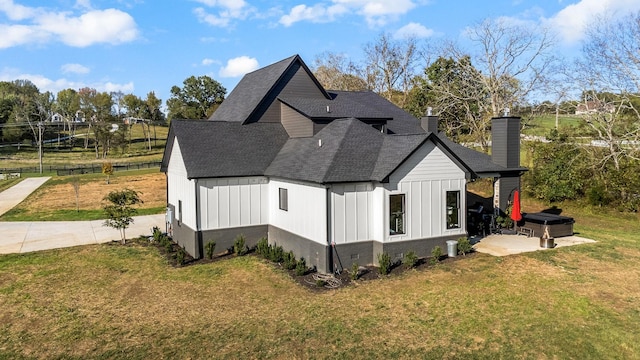 view of side of home with a patio, roof with shingles, a yard, a chimney, and board and batten siding