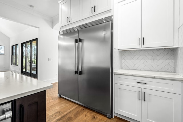 kitchen with light stone countertops, light wood-style flooring, white cabinets, built in refrigerator, and tasteful backsplash