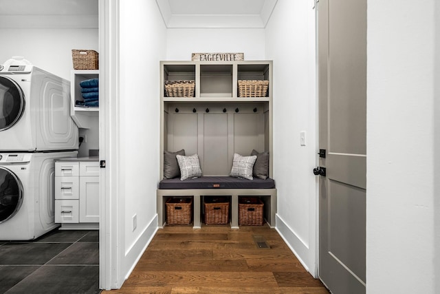 laundry room featuring dark wood-type flooring, baseboards, ornamental molding, stacked washing maching and dryer, and cabinet space