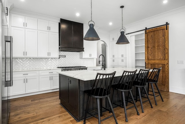 kitchen featuring dark wood-style floors, a center island with sink, a sink, custom range hood, and white cabinets