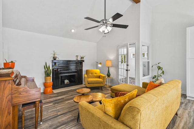 living room featuring ceiling fan, high vaulted ceiling, a fireplace with raised hearth, and wood finished floors