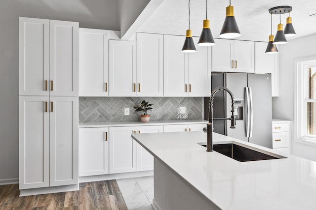 kitchen featuring pendant lighting, a sink, tasteful backsplash, stainless steel fridge, and white cabinets