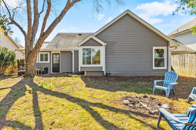 back of house featuring fence, an outdoor fire pit, roof with shingles, a lawn, and cooling unit