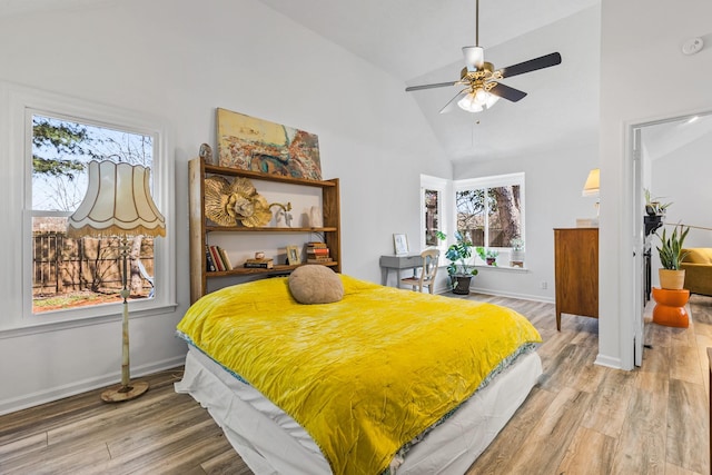 bedroom with ceiling fan, light wood-style floors, baseboards, and high vaulted ceiling