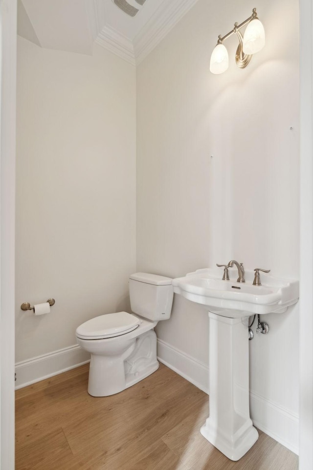 half bath featuring toilet, wood finished floors, baseboards, and ornamental molding