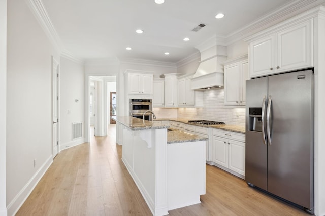 kitchen featuring visible vents, decorative backsplash, custom range hood, white cabinets, and appliances with stainless steel finishes