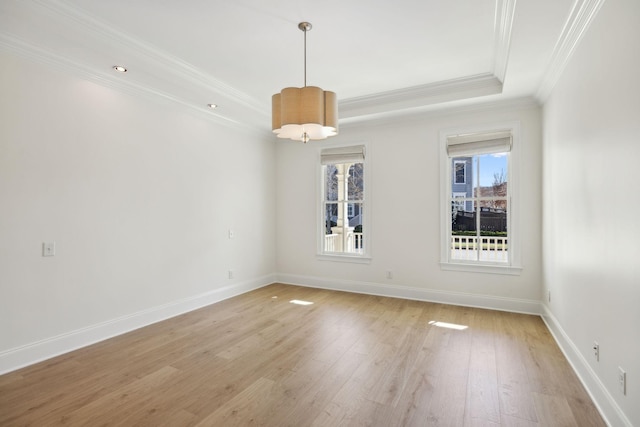 spare room featuring a tray ceiling, baseboards, and light wood finished floors