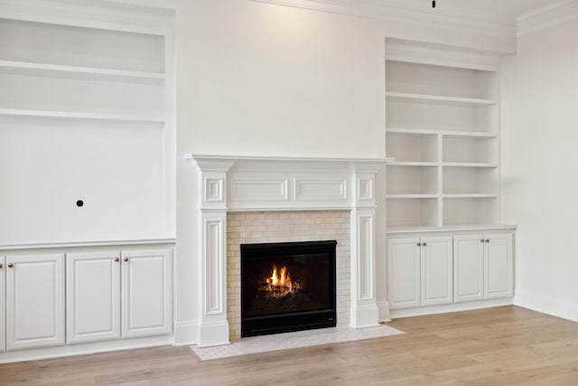 unfurnished living room with built in shelves, baseboards, light wood-style flooring, a fireplace with flush hearth, and crown molding