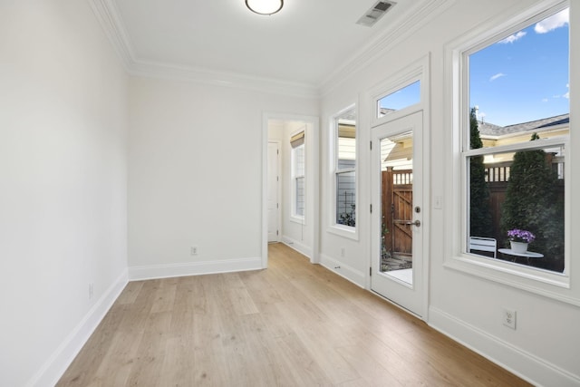 spare room featuring light wood-type flooring, visible vents, baseboards, and ornamental molding