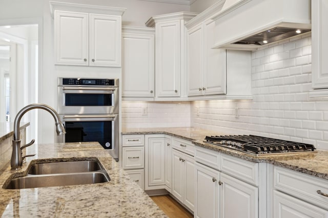 kitchen with a sink, backsplash, appliances with stainless steel finishes, white cabinets, and custom exhaust hood