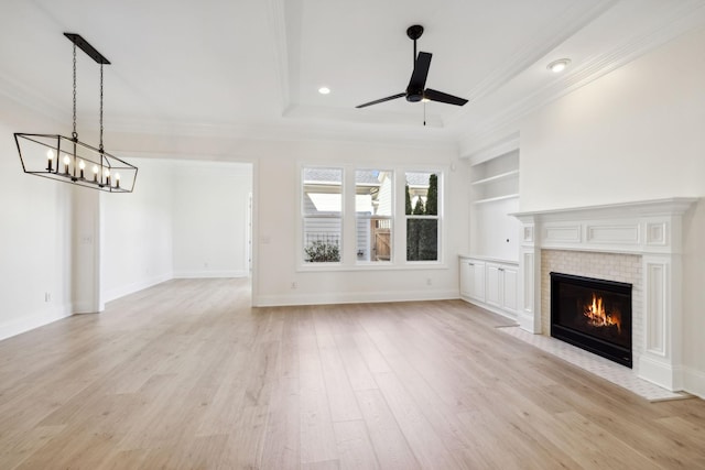 unfurnished living room featuring ornamental molding, ceiling fan with notable chandelier, built in features, light wood finished floors, and a tile fireplace