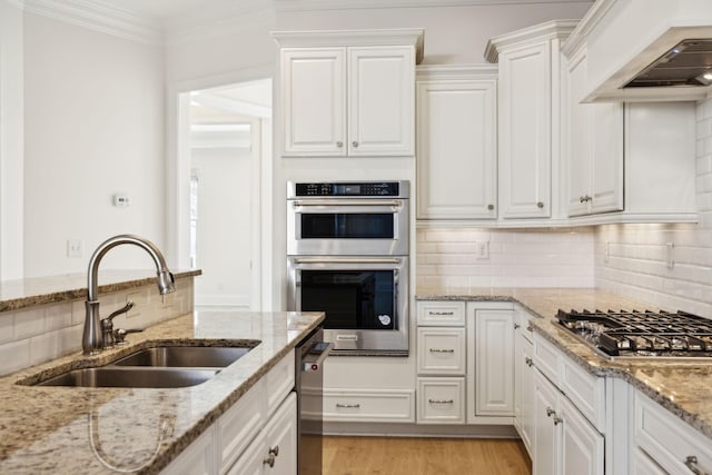 kitchen with a sink, light wood-style floors, appliances with stainless steel finishes, white cabinets, and wall chimney range hood