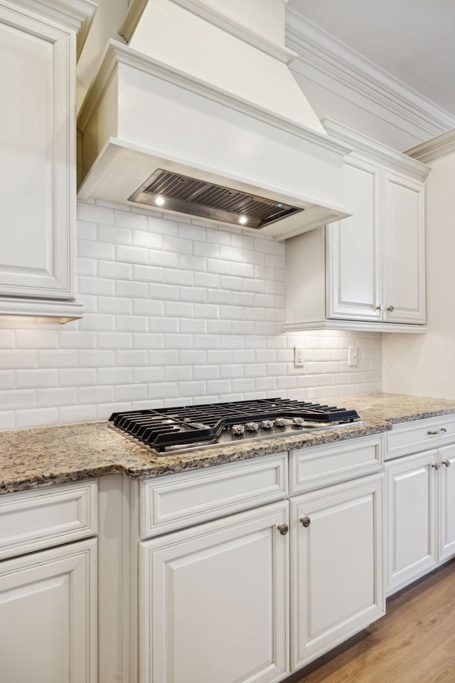 kitchen with premium range hood, ornamental molding, decorative backsplash, stainless steel gas stovetop, and white cabinetry