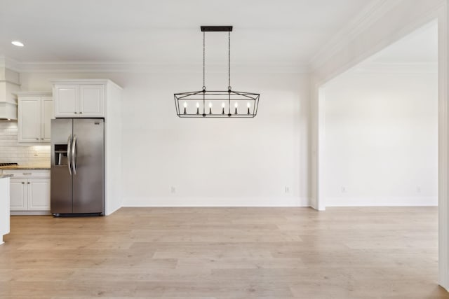 unfurnished dining area featuring light wood-type flooring, baseboards, a notable chandelier, and ornamental molding