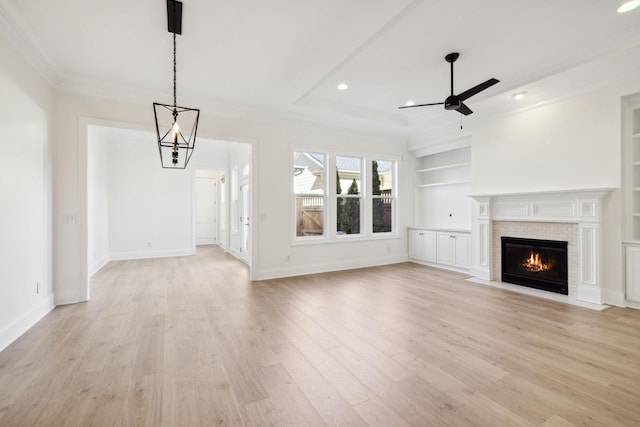 unfurnished living room featuring built in shelves, ornamental molding, a ceiling fan, light wood finished floors, and baseboards