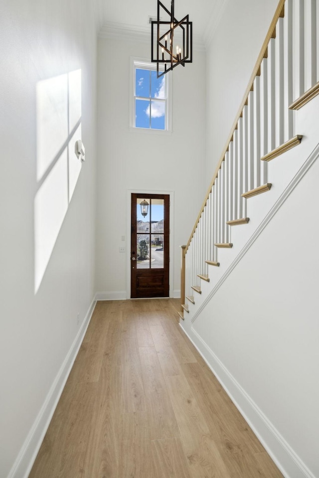 entryway with a notable chandelier, ornamental molding, wood finished floors, baseboards, and stairs