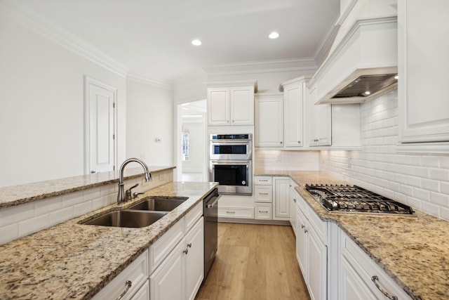 kitchen with premium range hood, light wood-type flooring, ornamental molding, stainless steel appliances, and a sink