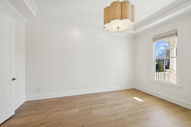 empty room with a raised ceiling, ornamental molding, light wood finished floors, baseboards, and a chandelier