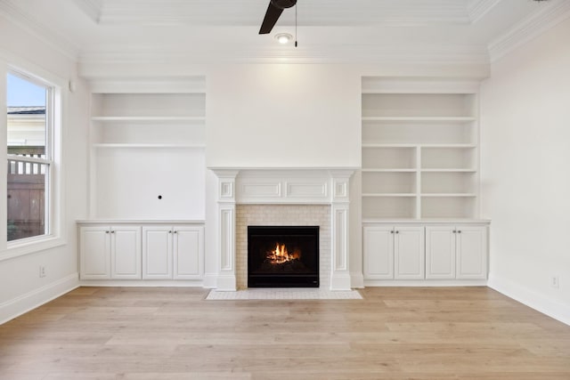 unfurnished living room featuring built in shelves, light wood-style floors, a fireplace, crown molding, and baseboards