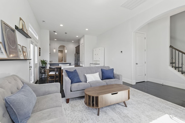 living area with stairway, wood finished floors, baseboards, recessed lighting, and arched walkways