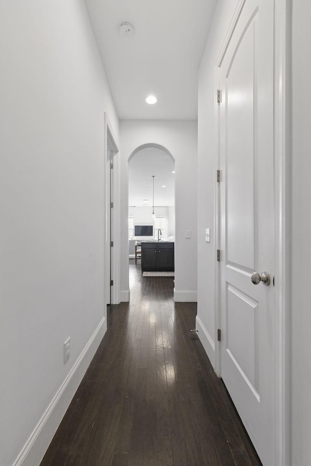 hall featuring dark wood-style floors, baseboards, recessed lighting, arched walkways, and a sink