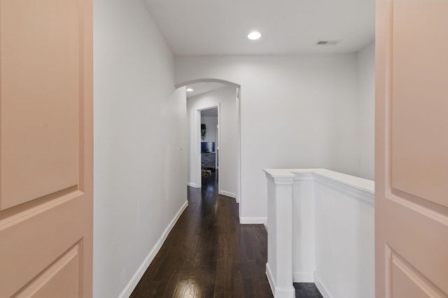 hallway with dark wood-style floors, visible vents, baseboards, arched walkways, and an upstairs landing