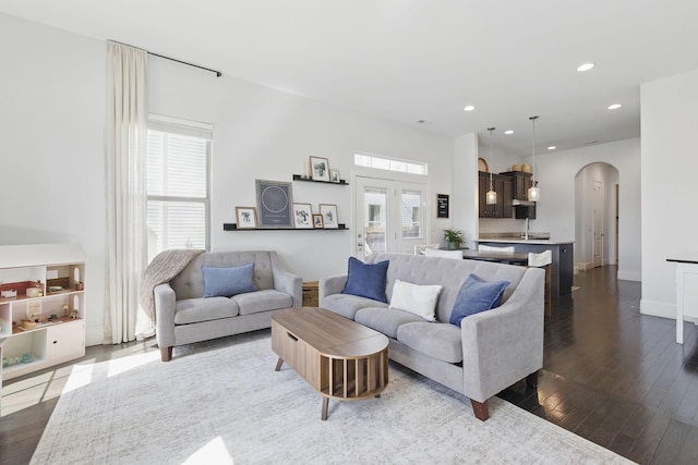 living room featuring recessed lighting, arched walkways, dark wood-style flooring, and baseboards