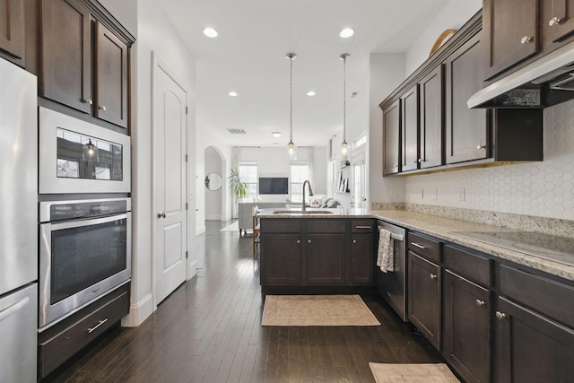 kitchen featuring a sink, dark brown cabinets, under cabinet range hood, appliances with stainless steel finishes, and open floor plan