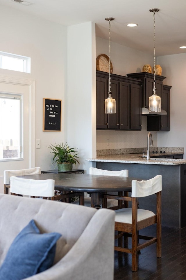 kitchen featuring dark wood-type flooring, pendant lighting, recessed lighting, dark brown cabinetry, and light stone countertops