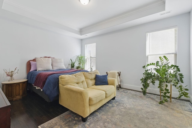 bedroom with baseboards, visible vents, a tray ceiling, wood-type flooring, and crown molding