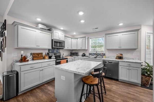 kitchen with a sink, stainless steel appliances, a kitchen breakfast bar, and dark wood finished floors